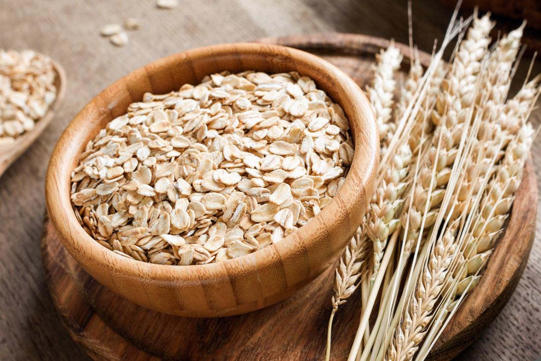 Rolled oat flakes into a wooden bowl, with flakes in a wooden spoon, together with its branches