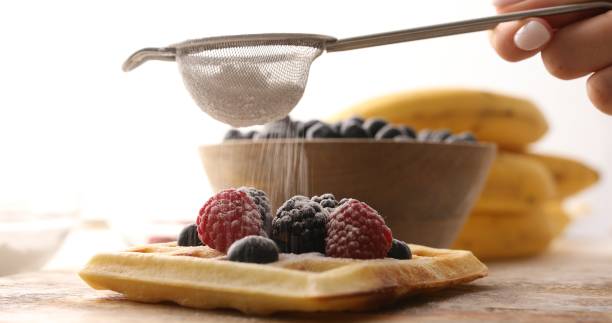 O açúcar em pó é polvilhado em um waffle belga com frutas vermelhas.